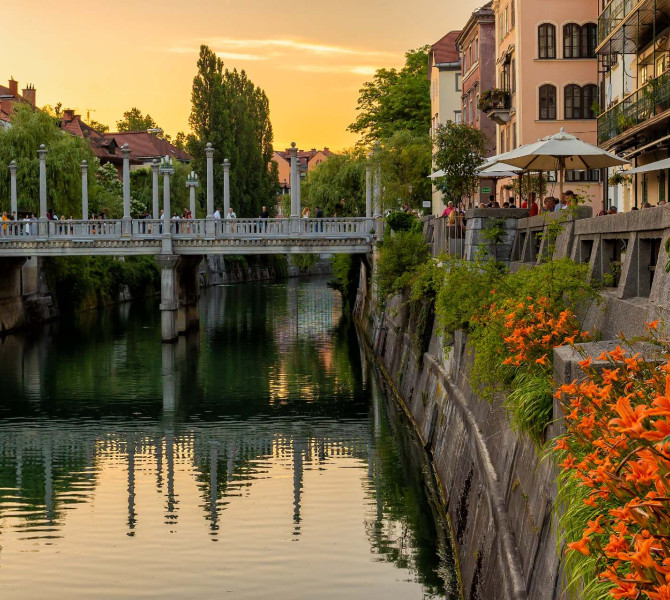 Reka in kamnito nabrežje polno rož, čez reko most.