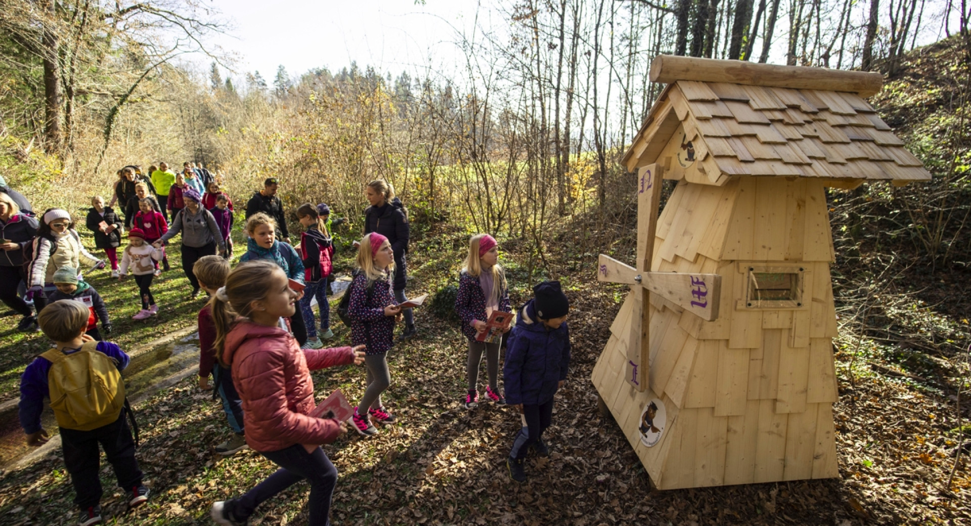 Otroci pred lesenim pomanjšanim mlinom na veter v gozdu.