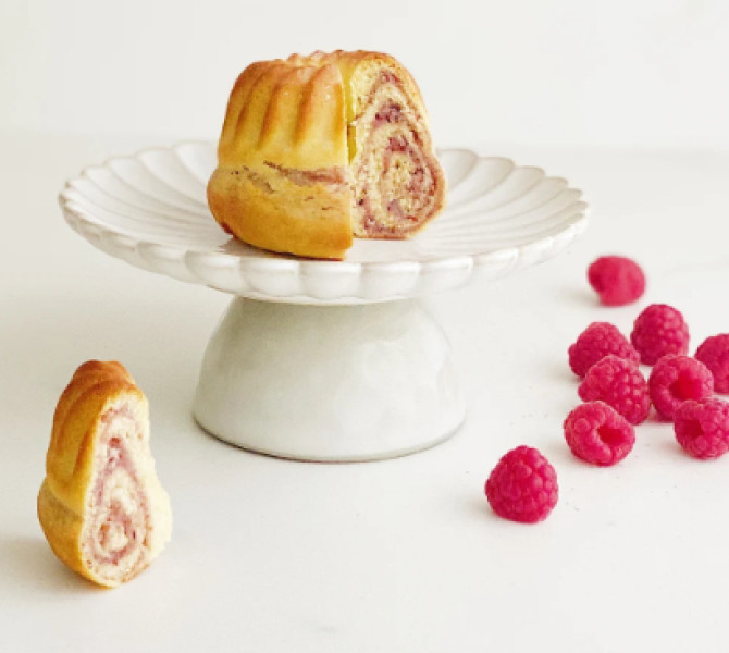 Majhna potica z okusom maline na belem krozniku, ob njem maline.