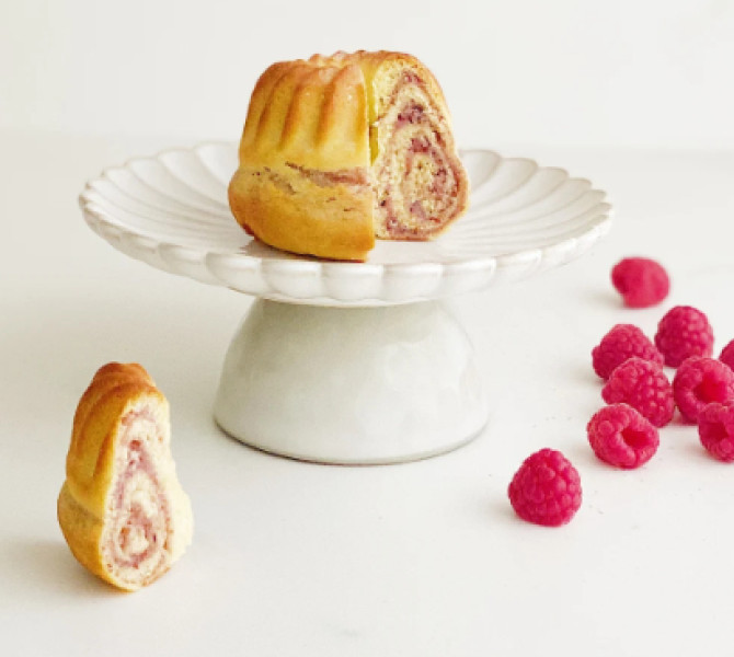 Majhna potica z okusom maline na belem krožniku, ob njem maline.