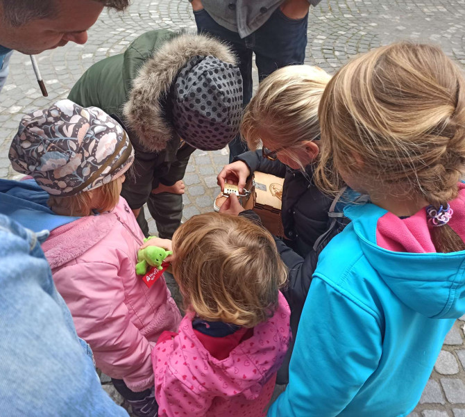 Otroci stojijo v krogu in odpirajo ključavnico na leseni škatli.