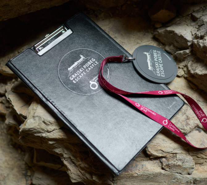 Črna mapa in okrogli obesek z logom Ljubljanskega gradu.