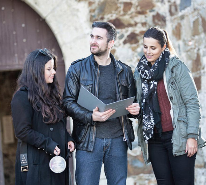 Trije ljudje si ogledujejo črno mapo z navodili za igranje igre. 