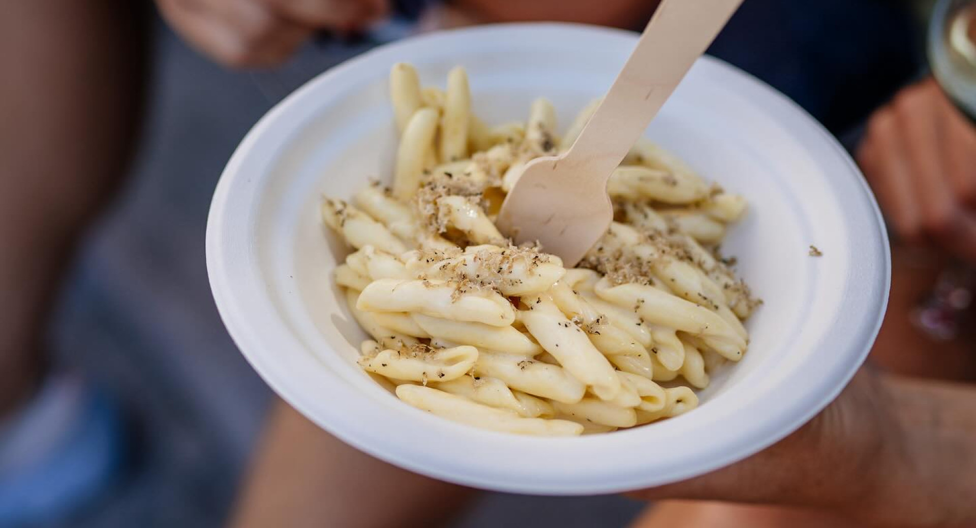 Weiße Trofie-Pasta mit geriebenen Trüffeln, serviert in einer weißen Schale mit einer Holzgabel.