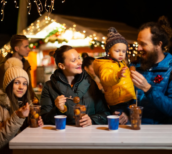 Una giovane famiglia sta gustando bevande calde all'aperto, con una bancarella dietro di loro.