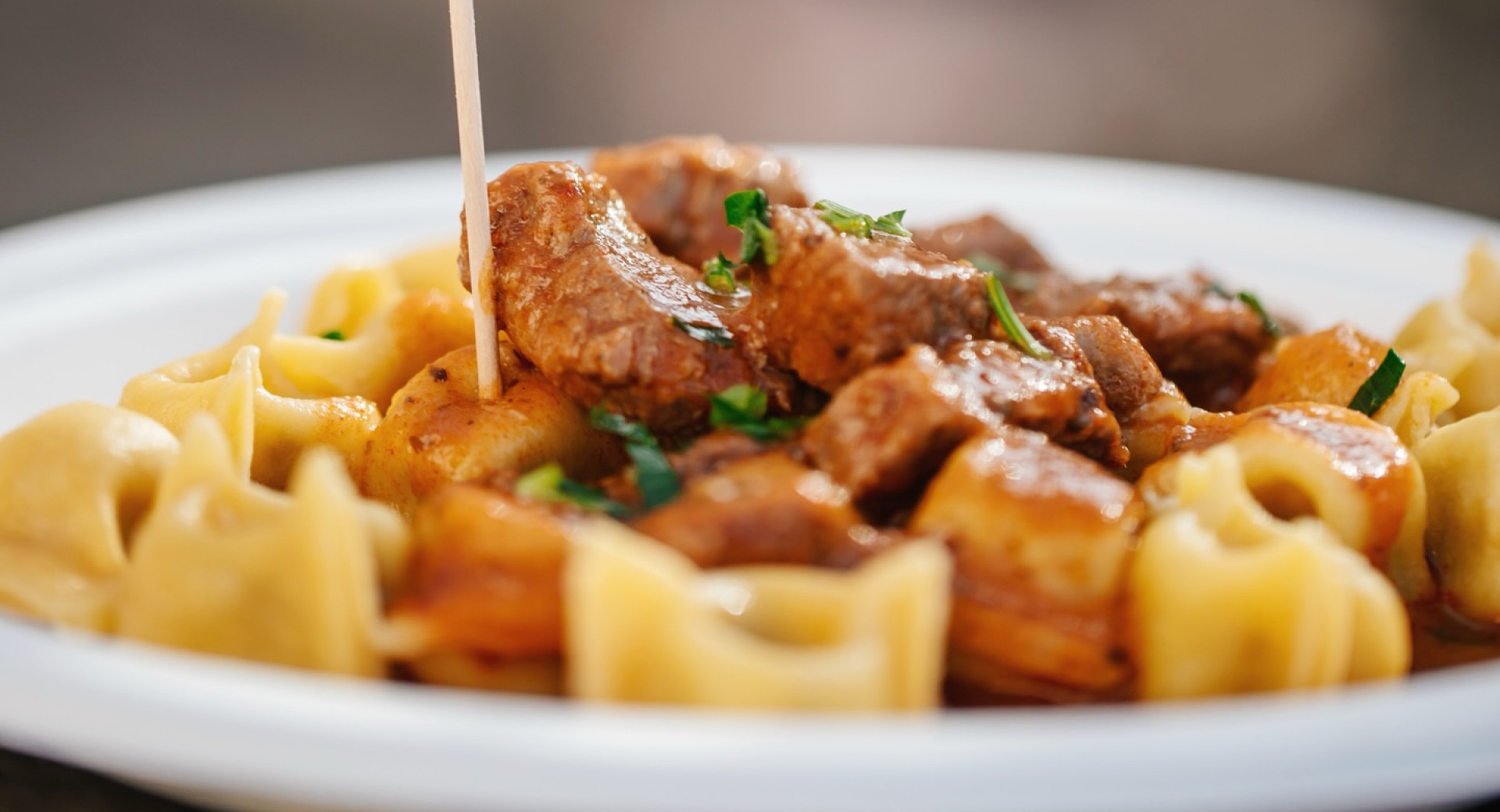 Idrija Žlikrofi auf einem weißen Teller, überzogen mit einer kräftigen Fleischsauce und mit frischer Petersilie bestreut.