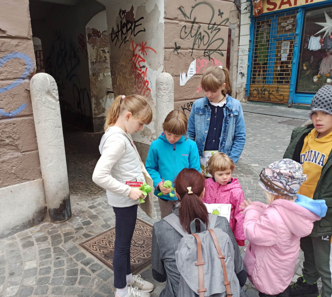 Otroci in stars stojijo v krogu in gledajo brosuro v starem mestnem jedru.