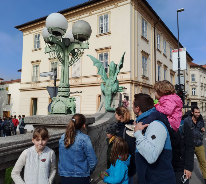 Starsi in otroci si ogledujejo kip zmaja na Zmajskem mostu. 