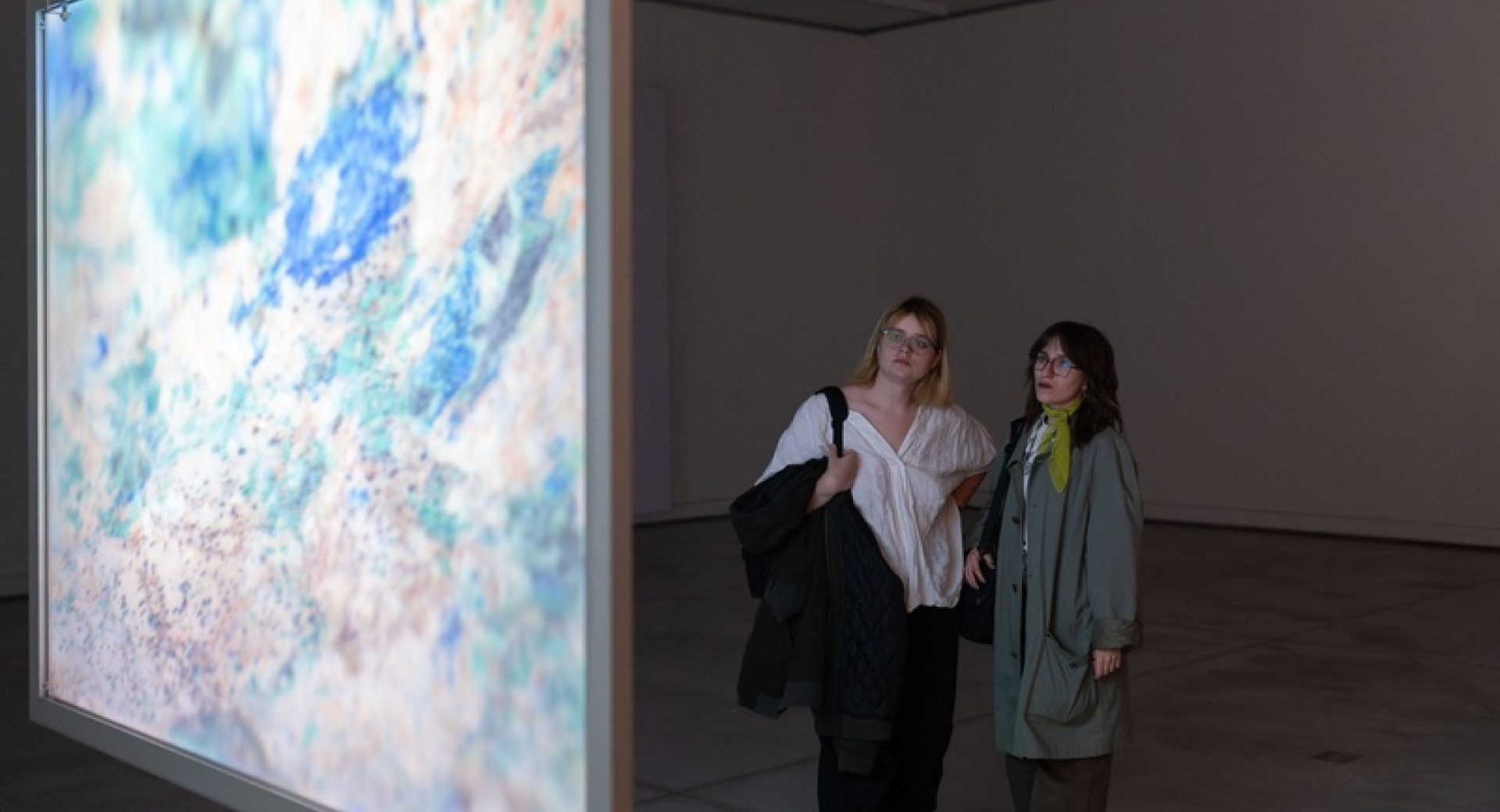 Two female visitors are viewing an exhibition on a large display board in a spacious hall.