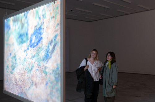 Two female visitors are viewing an exhibition on a large display board in a spacious hall.