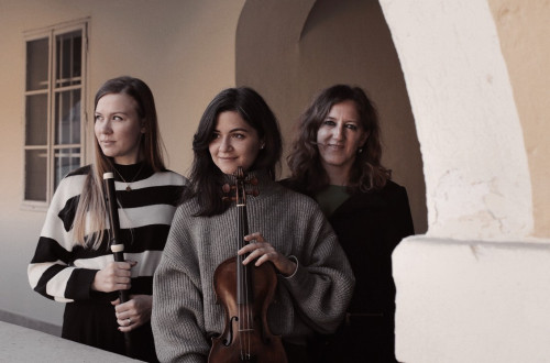 Three women holding instruments are standing under a stone arch.