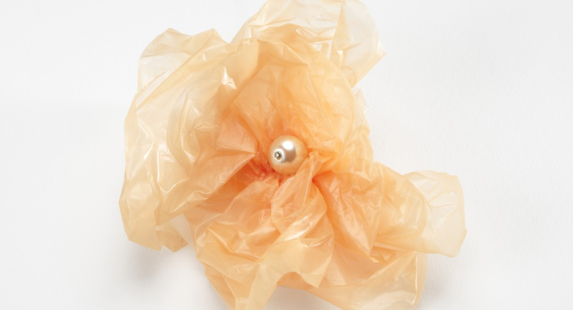 Fotografija bisera v oranzni zmeckani plastiki na belem ozadju.