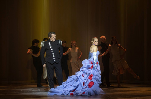 Svetlolasa zenska v dolgi svetlo modri obleki in moski v crni obleki na odru.