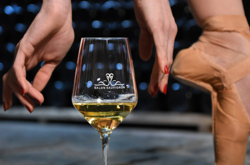 A glass of white wine next to a ballerina’s leg.
