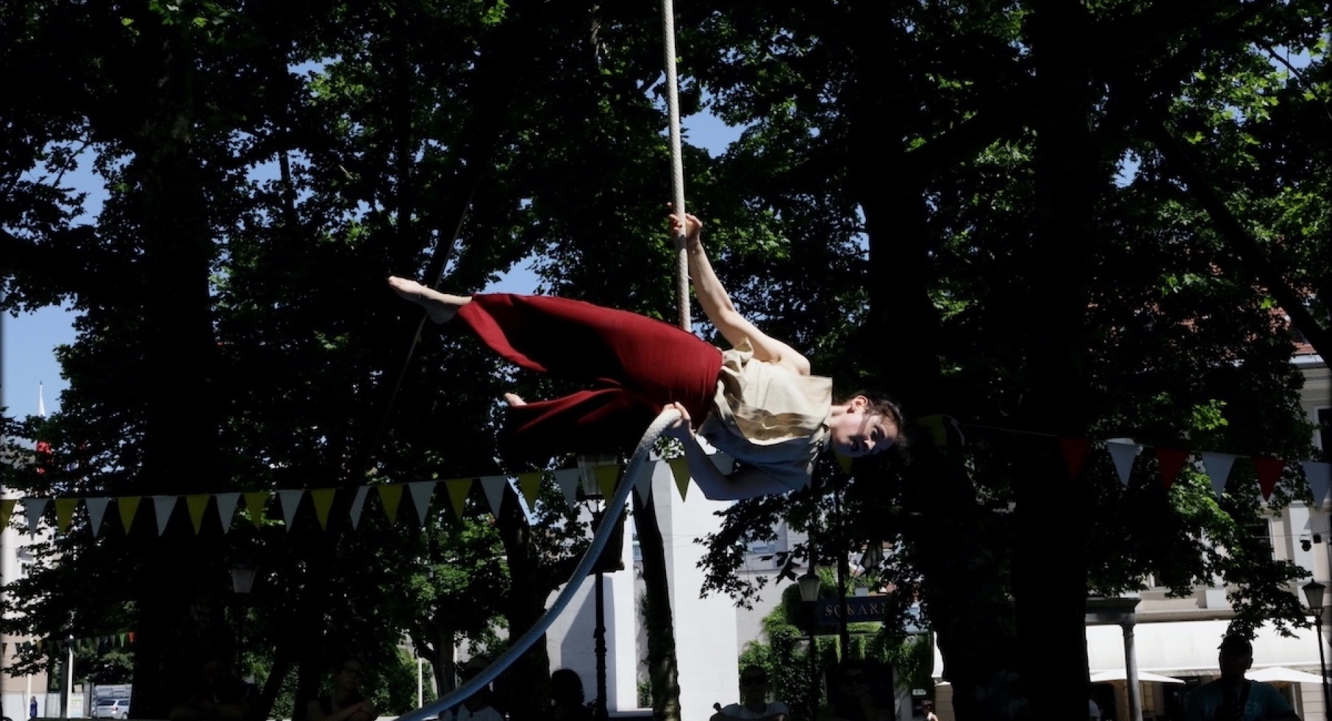 A female circus performer is doing aerial acrobatics, suspended by a rope.