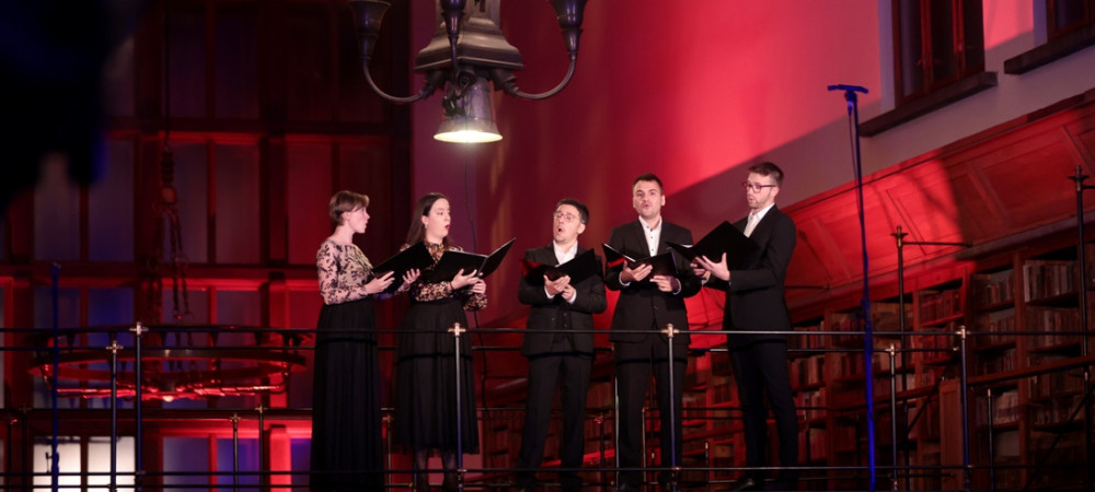 A group of singers on a high stage, with red lighting in the background.