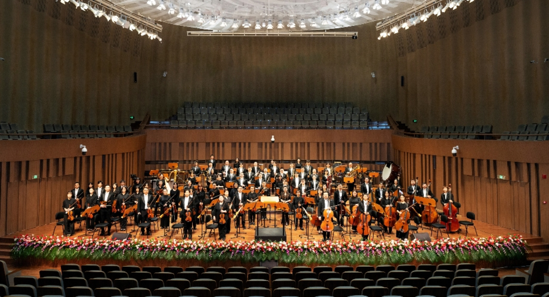 An orchestra in a grand hall with white lights.