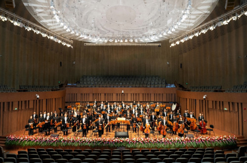 An orchestra in a grand hall with white lights.