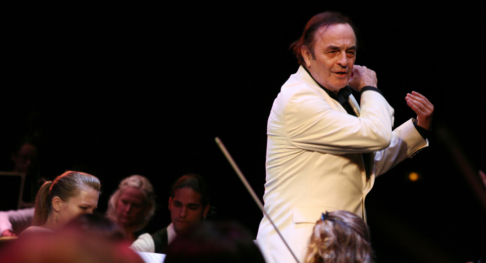 The conductor in a white suit is conducting the orchestra below him.