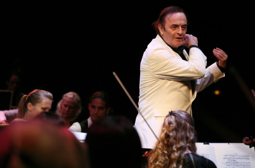 Dirigent v belem suknjicu dirigira orkester, ki je pod njim.