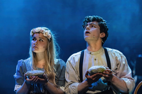 Fant in dekle nastopata na odru, v rokah drzita vsak po en hlebec kruha in oba gledata desno navzgor.