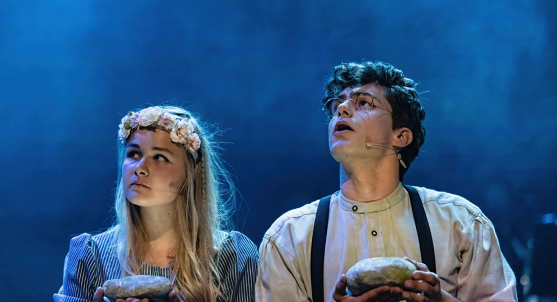 Fant in dekle nastopata na odru, v rokah drzita vsak po en hlebec kruha in oba gledata desno navzgor.