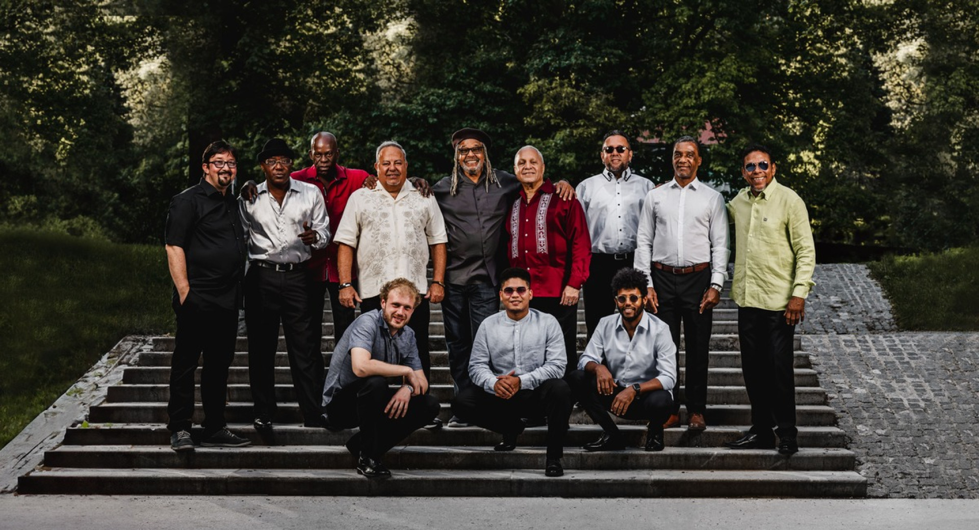 A Slovenian-Cuban music group poses for a photo on stone steps in an open-air setting.