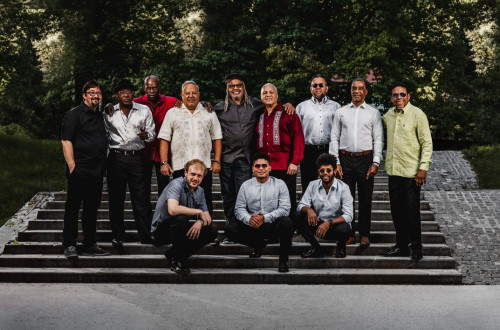 A Slovenian-Cuban music group poses for a photo on stone steps in an open-air setting.
