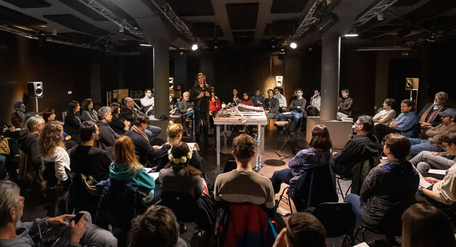 Skupina ljudi sedu v krogu okoli cloveka z mikrofonom.