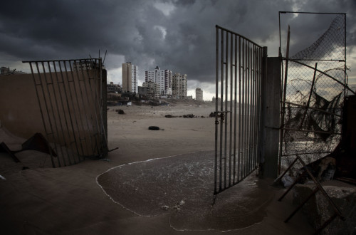 Stanovanjski bloki se dvigajo za zlomljenimi vrati obmorske restavracije. Gaza, 2011.