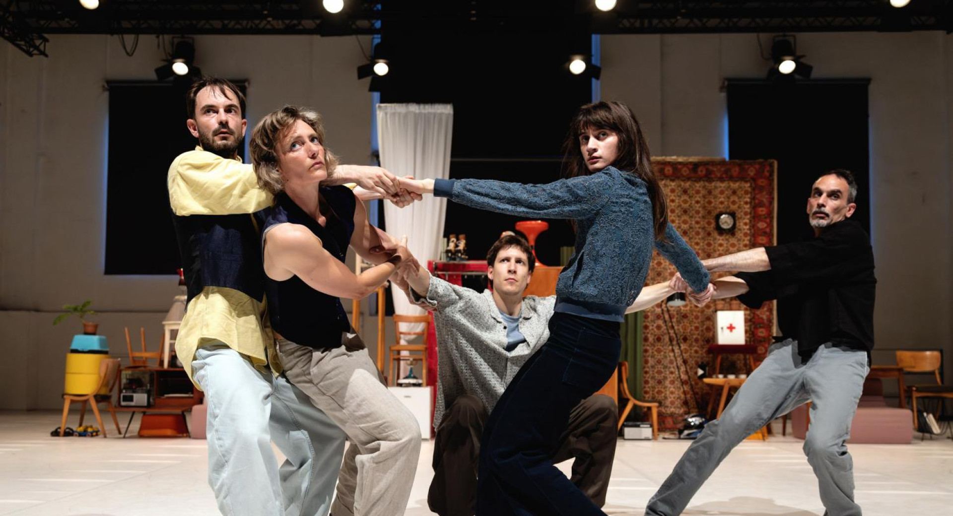 V notranjosti prostora se pet ljudi drzi za roke, vsak stoji v svoji plesni pozi.