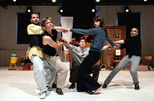 V notranjosti prostora se pet ljudi drzi za roke, vsak stoji v svoji plesni pozi.