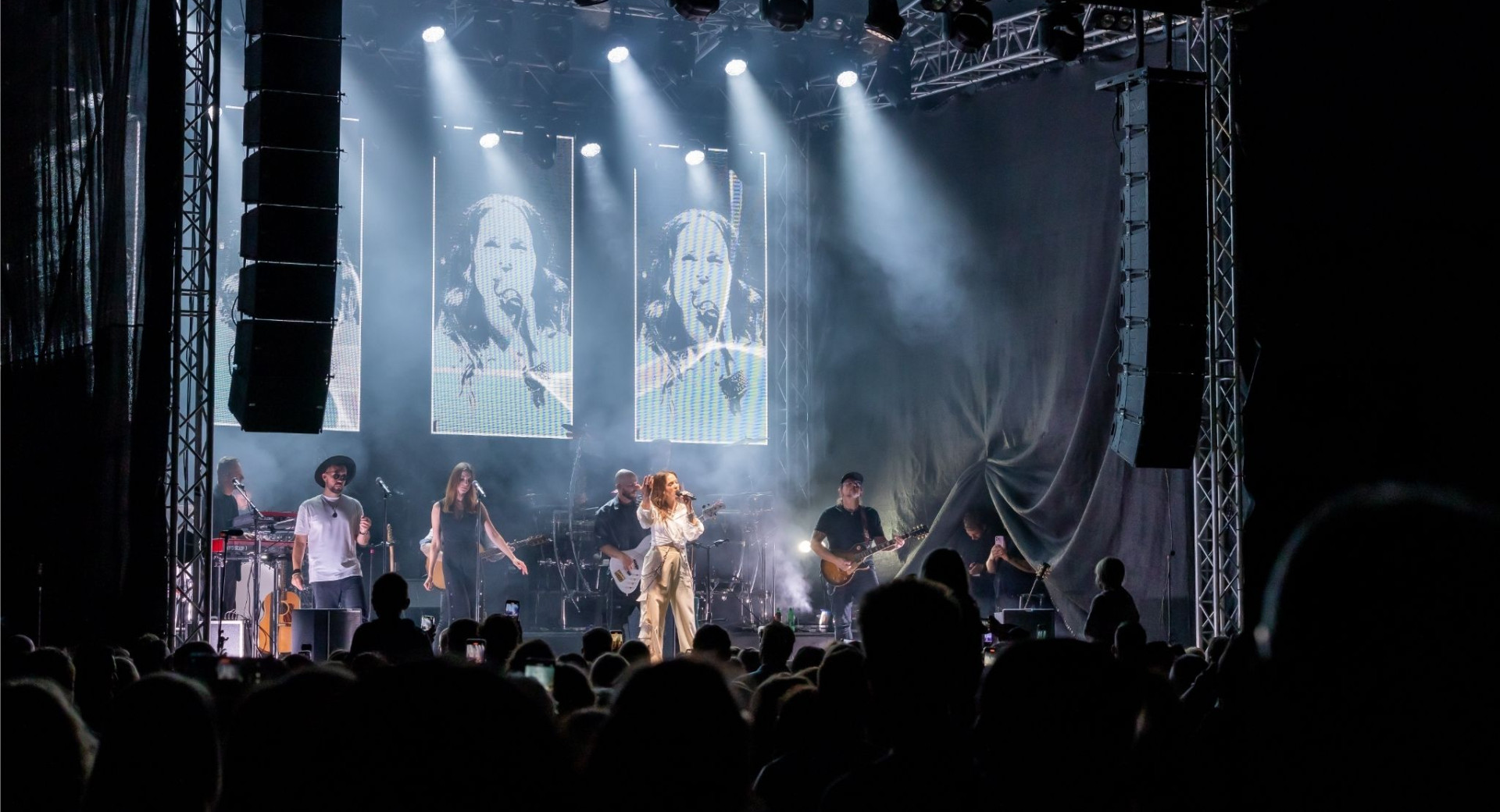 A singer and a band are performing on a lit-up stage.