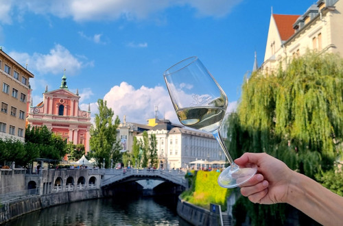 A person holding a glass of white wine with a view of Ljubljana's historic city center