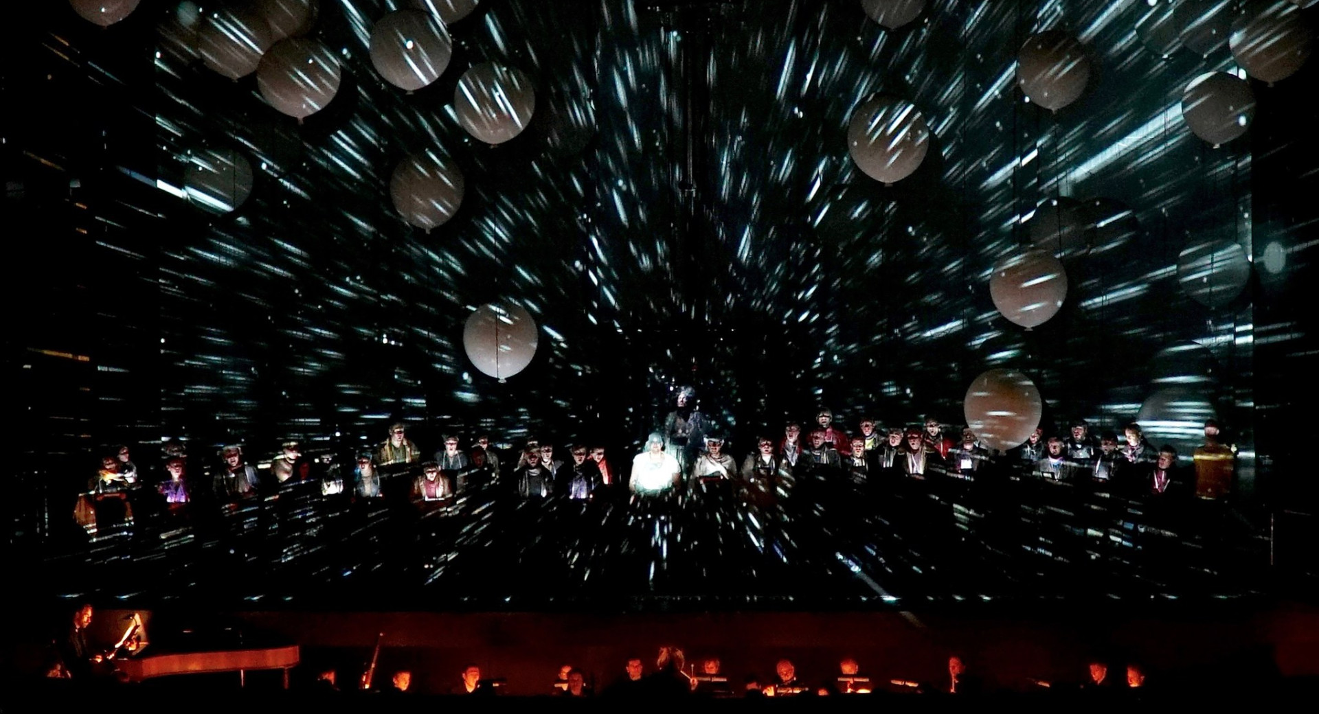 A group of people on stage with a dark background and white balloons.