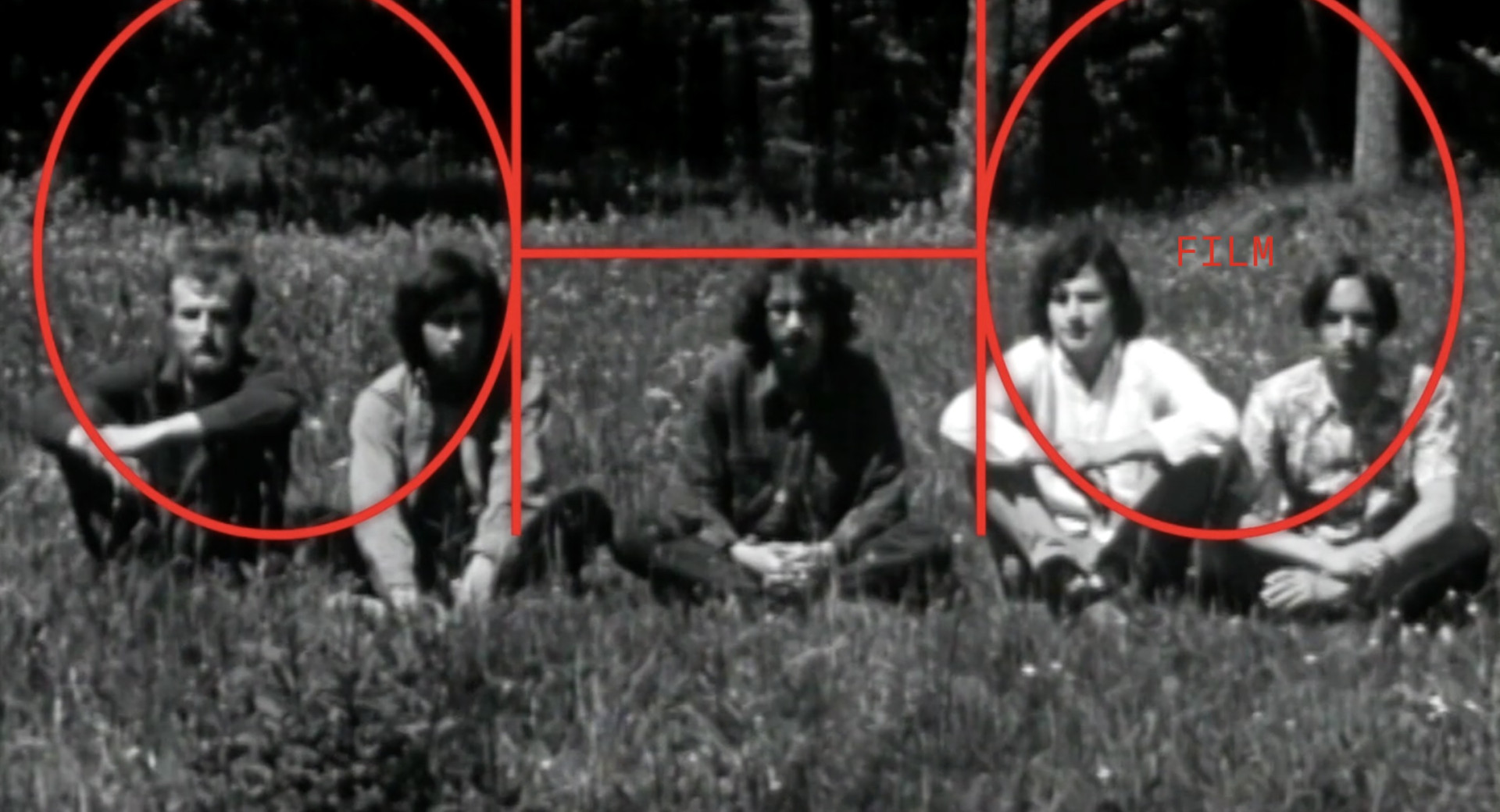 Stara crno-bela fotografija petih moskih, ki sedijo v vrsti na travniku, za njimi pa so drevesa.