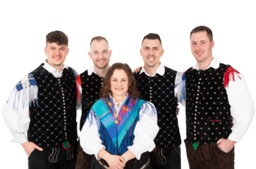 Stirje moski in ena zenska pred njimi stojijo, obleceni v slovenske narodne nose, in pozirajo za fotografijo pred belim ozadjem.