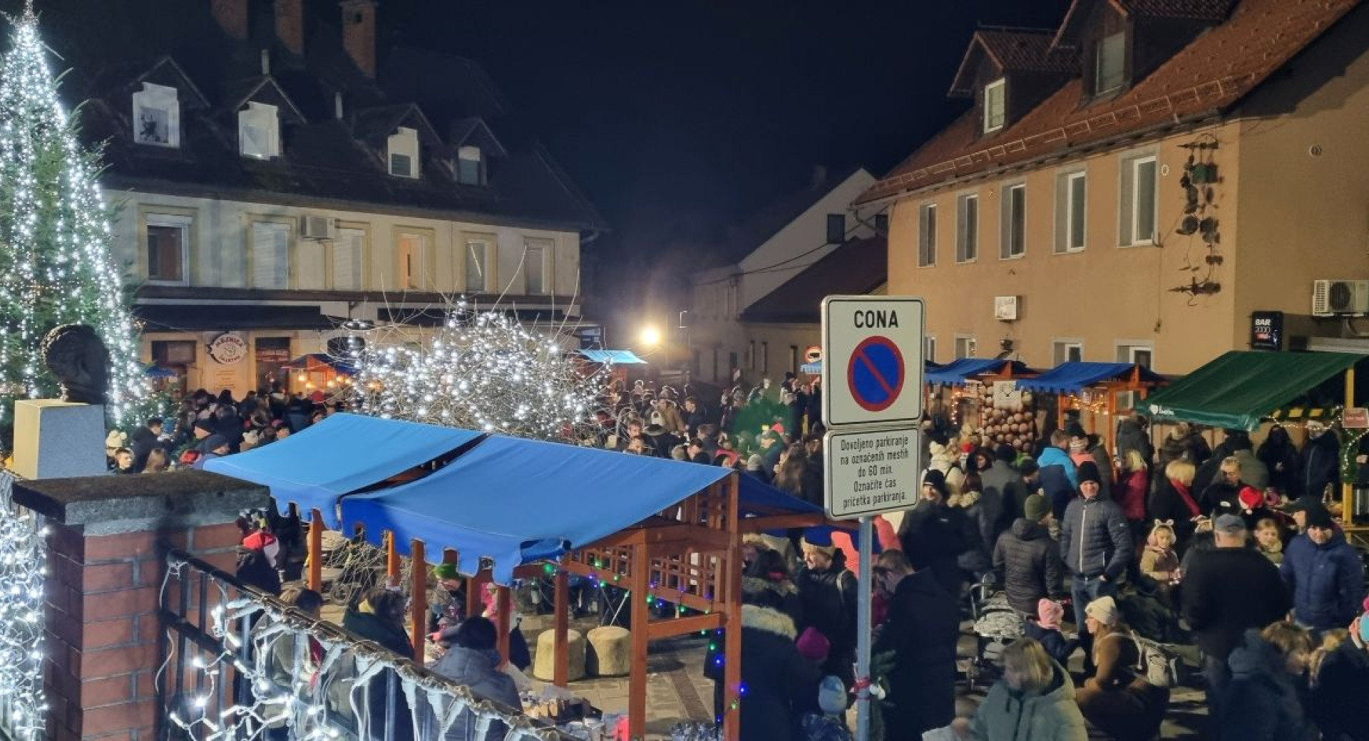 Ljudje se druzijo na prostem v praznicno okrasenem mestu ob stojnicah.
