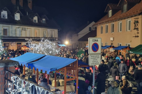 Ljudje se druzijo na prostem v praznicno okrasenem mestu ob stojnicah.