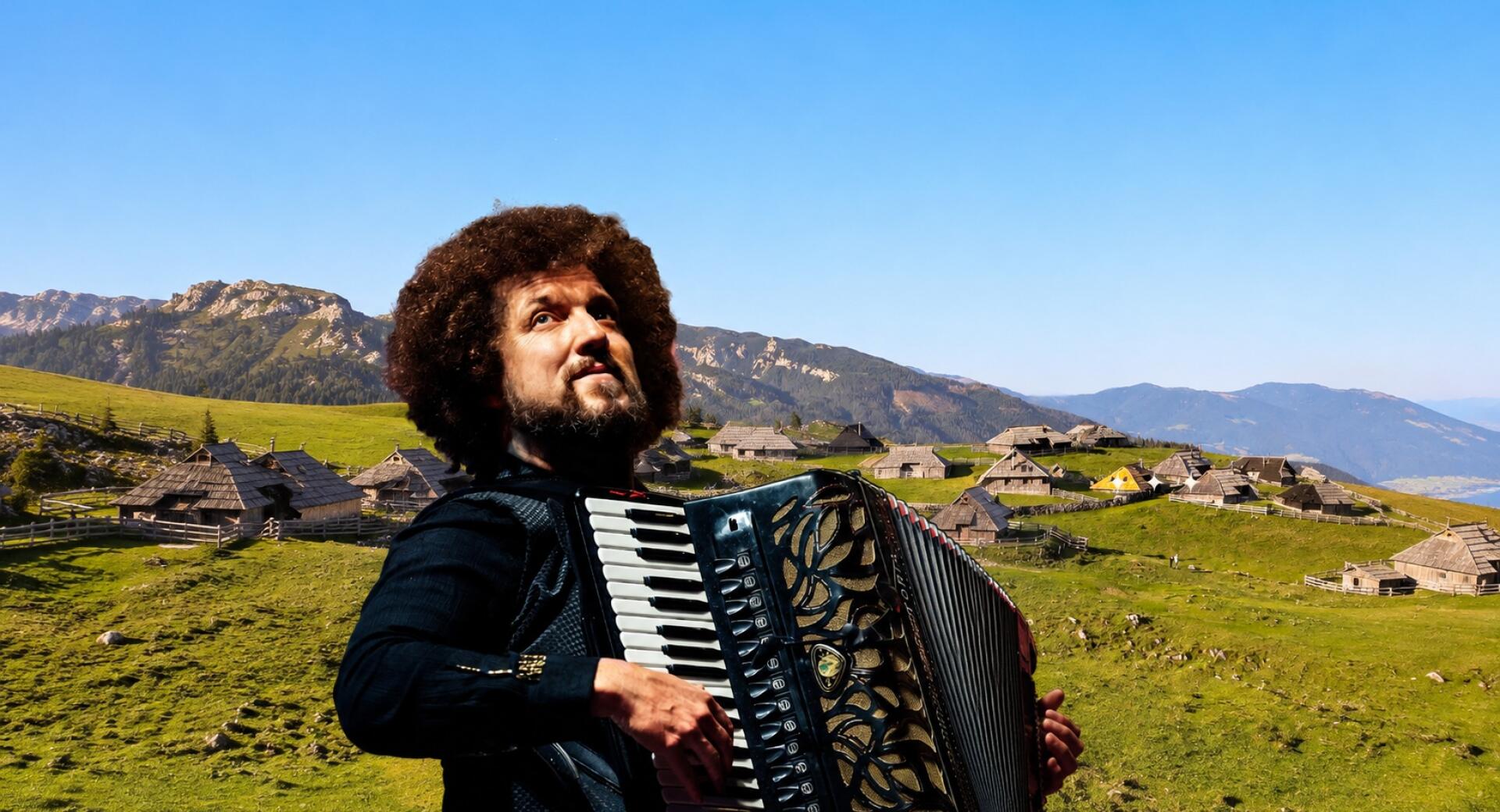 A man is playing the accordion in front of a green landscape with wooden houses and mountains in the background.