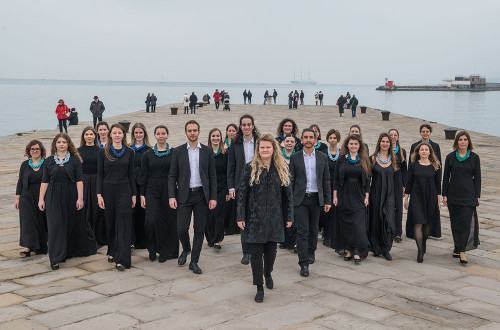 A group of people in black clothes standing on a large pier with the sea in the background.