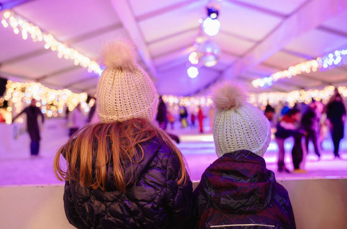 Punca in fant s kapama na glavi sta s hrbtom obrnjena proti kameri in gledata proti drsaliscu, ki je v ozadju fotografije.