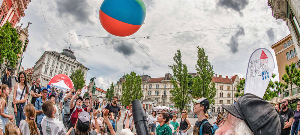 A group of children and parents observing an experiment with an inflatable ball at Preseren trg Square.
