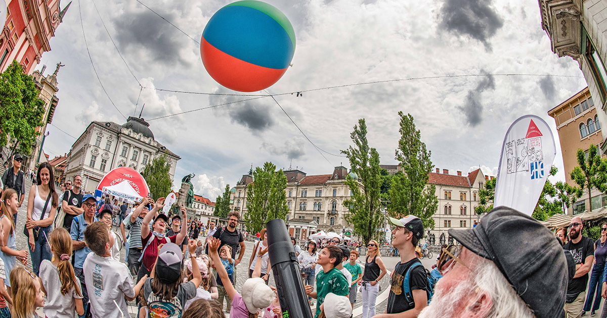 A group of children and parents observing an experiment with an inflatable ball at Preseren trg Square.