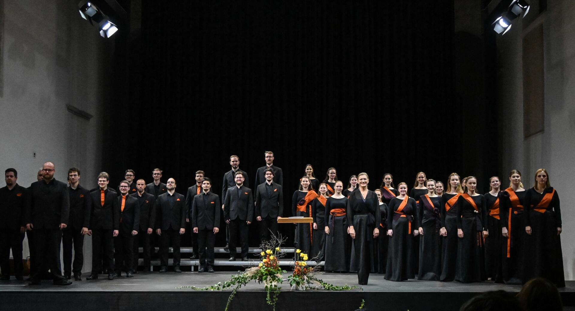 A choir dressed in black on stage in a dim hall.
