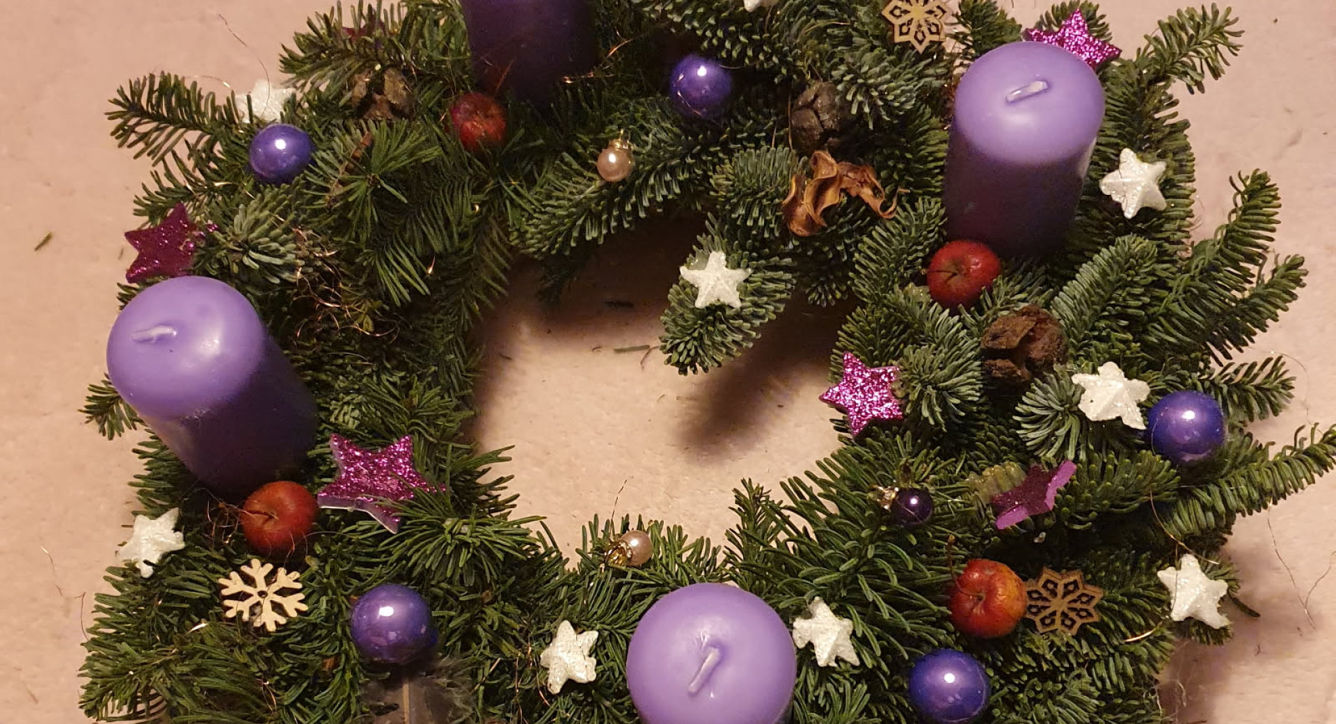 Adventni vencek iz naravnih materialov, okrasen z vijolicnimi sveckami, kroglicami, zvezdicami in snezinkami.