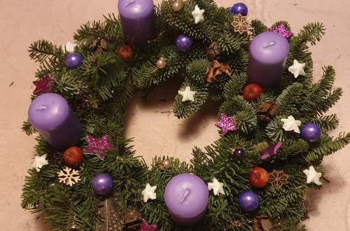 Adventni vencek iz naravnih materialov, okrasen z vijolicnimi sveckami, kroglicami, zvezdicami in snezinkami.