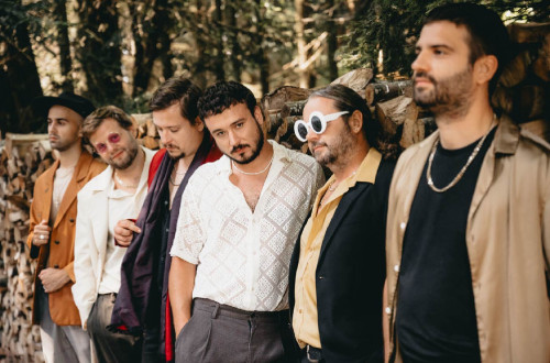 Skupina moskih pozira za fotografijo, kjer stojijo eden poleg drugega, v ozadju so pa drevesa.