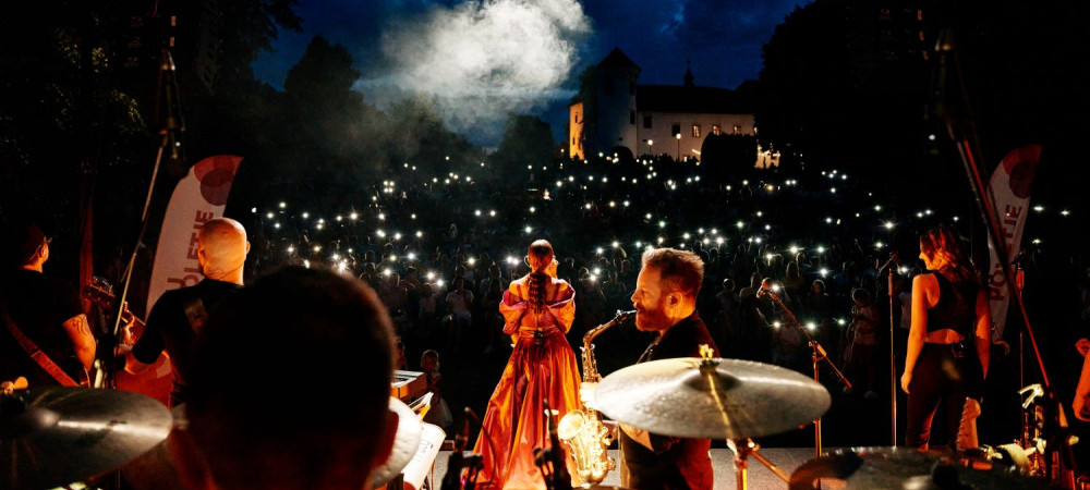 In a nighttime setting, the singer and the band are on stage from behind, with the audience in front holding small lights in their hands.