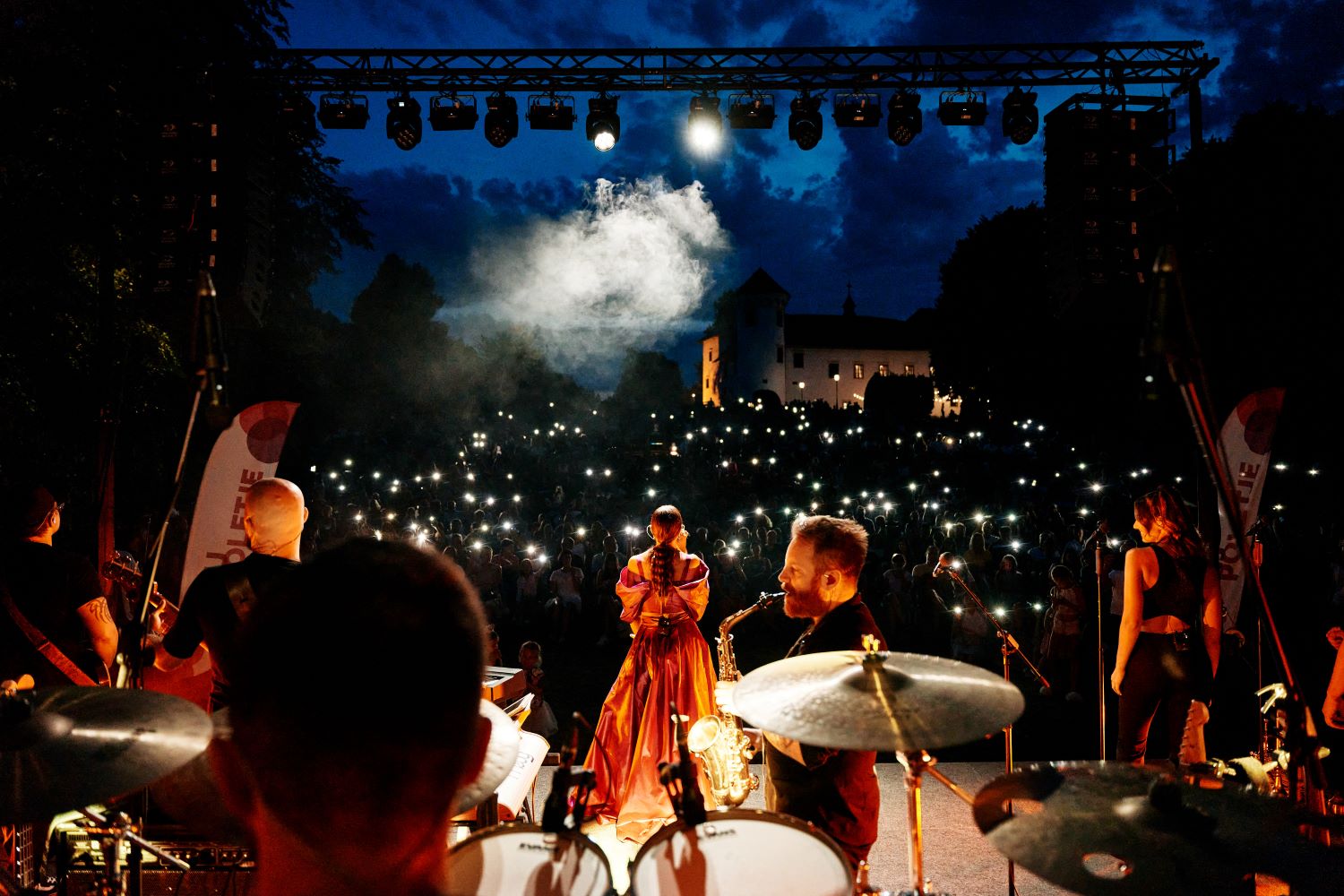 In a nighttime setting, the singer and the band are on stage from behind, with the audience in front holding small lights in their hands.